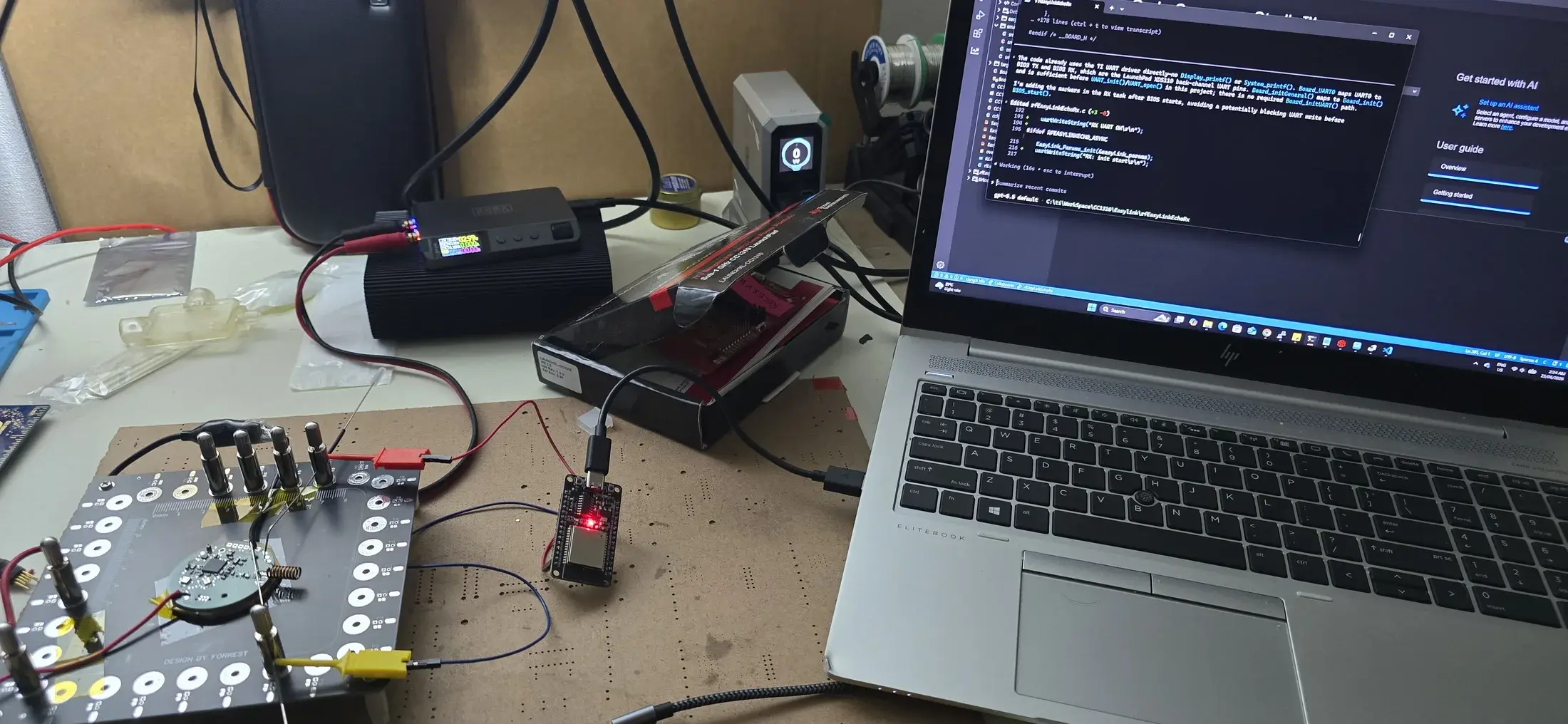 Custom sensor hardware and development boards connected beside a laptop displaying embedded firmware source code.